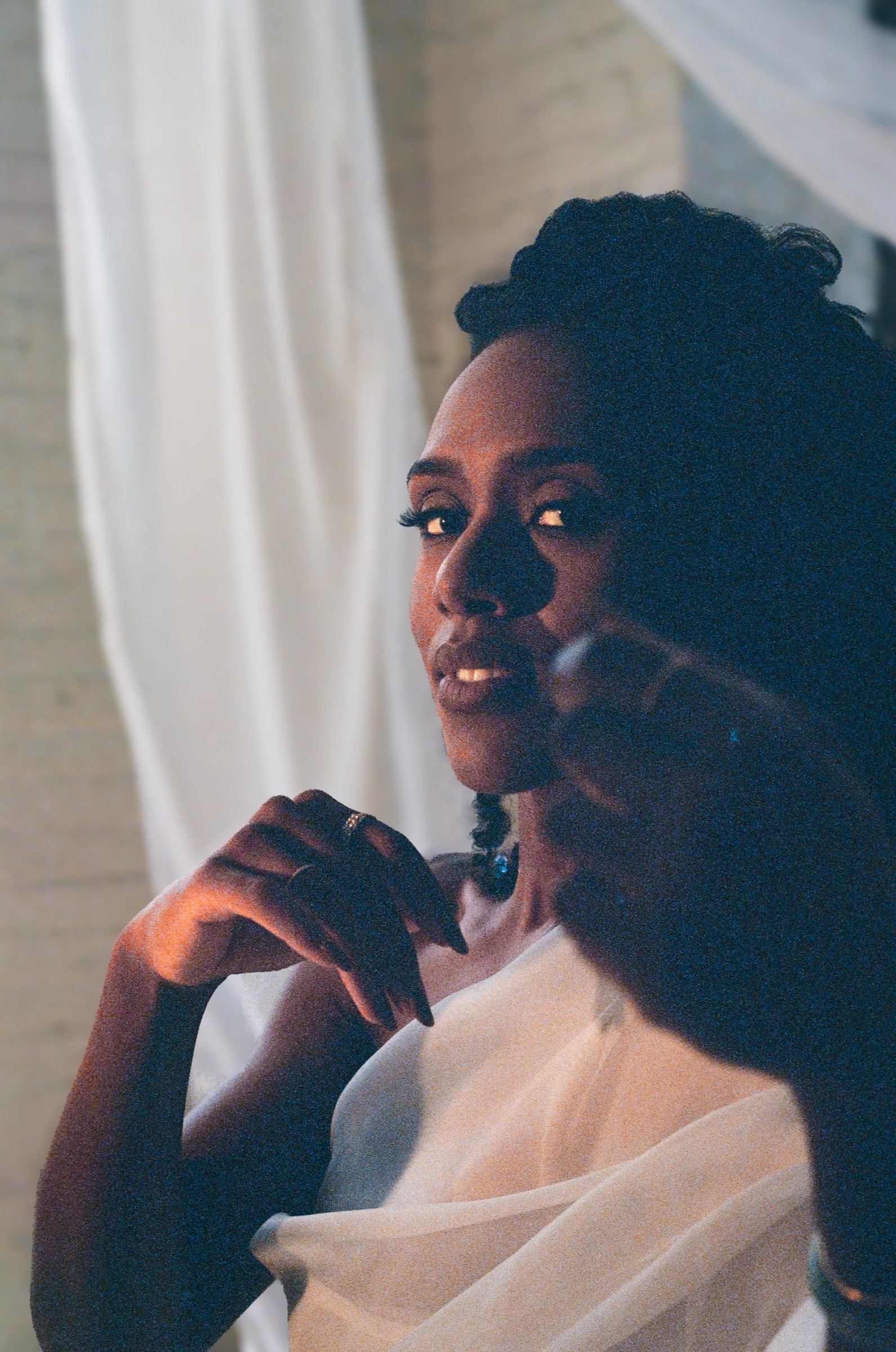 Alicia Waller backlit against a white curtain, holding a microphone, in warm amber light.