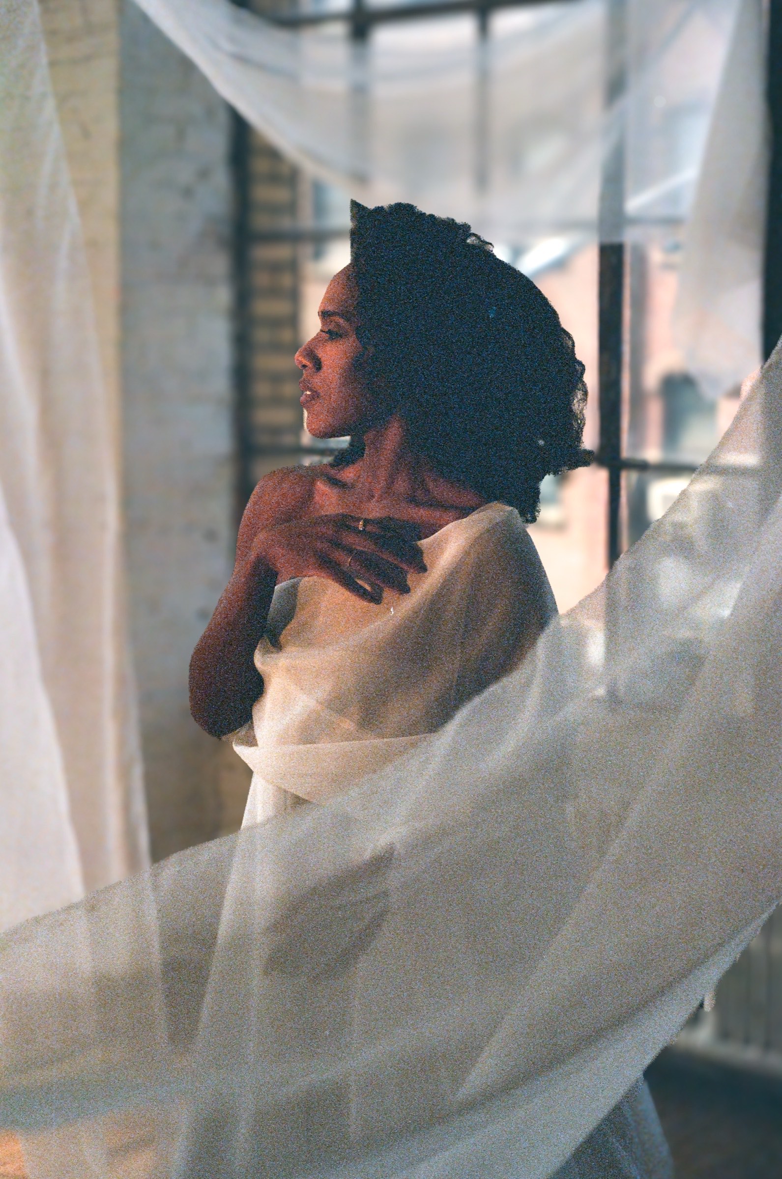 Alicia Waller beside a window draped in sheer fabric, in warm daylight.